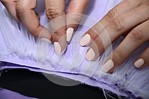 A woman attaches cambric cloth to satin fabric. Seamstress collects lilac fabric closeup