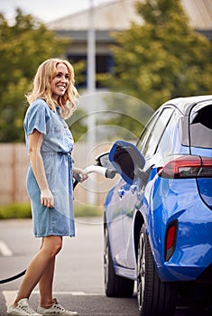 Woman Attaching Charging Cable To Environmentally Friendly Zero Emission Electric Car Outdoors