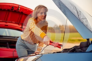 Woman Attaching Jumper Cable To Start Car Engine With Flat Battery