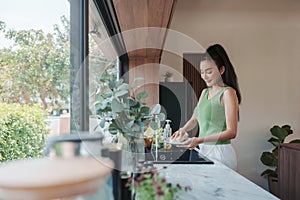Woman attentively scrubbing dishware in a kitchen with greenery