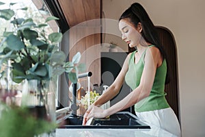 Woman attentively scrubbing dishware in a kitchen with greenery