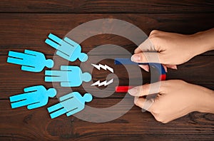 Woman attracting paper people with magnet at table, top view