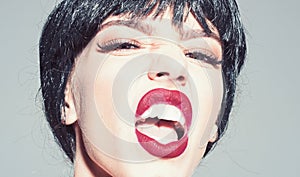 Woman with attractive red lips shouting. Lady in black wig with make up on grey background. Scandalous lady concept photo