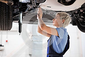 Woman auto mechanic fixing car, mechanic repairing car on lift in garage. side view