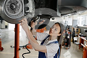 Woman auto mechanic fixing running gear of car at service station