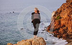 Woman in autumn fashion dress on the ocean coast, on rocky beach.