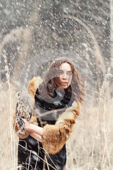 Woman in autumn in fur coat with owl on hand first snow. Beautiful brunette girl with long hair in nature, holding an owl.