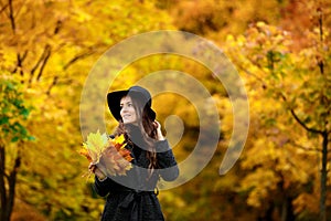 Woman with autumn leaves in hand and fall yellow maple garden background