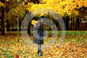 Woman with autumn leaves in hand and fall yellow maple garden background