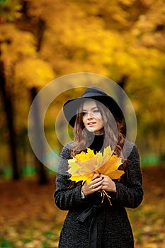 Woman with autumn leaves in hand and fall yellow maple garden background