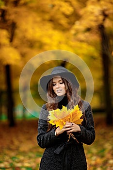 Woman with autumn leaves in hand and fall yellow maple garden background