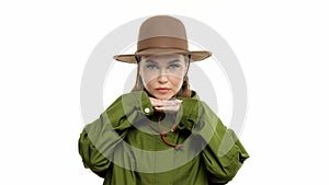 Woman in a autumn look in studio in green parka and hat turns and poses to the camera