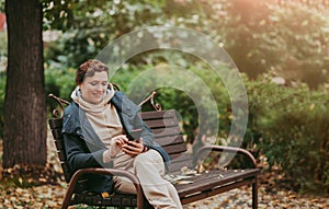 A woman in an autumn park reads messages in a smartphone