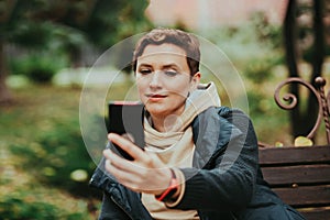 A woman in an autumn park reads messages in a smartphone