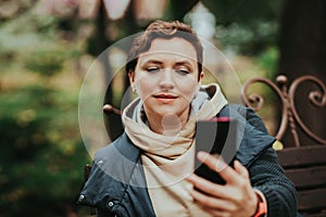 A woman in an autumn park reads messages in a smartphone