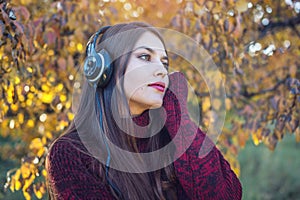 Woman in autumn Park standing listening to music with her headphones. Concept of good mood, favorite music, happy time.