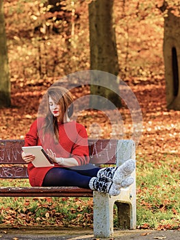 Woman in autumn park using tablet computer reading.