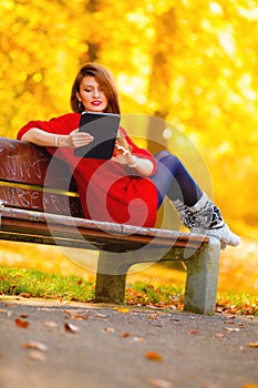 Woman in autumn park using tablet computer reading.