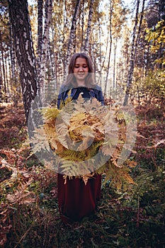 Woman autumn portrait. cute girl outdoors with a bouquet of yellow fern in the forest, autumn fall concept.