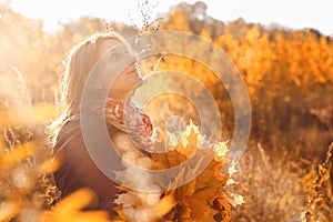 A woman in the autumn sun looks up. Girl holding a wreath of autumn leaves at sunset