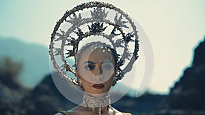 Woman with avant-garde headpiece and makeup posing in a dramatic outdoor setting