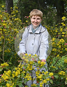 The woman of average years costs among the blossoming bushes of a trailing mahonia