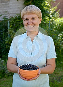 The woman of average years holds in hand a bowl with black currant