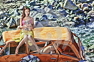 Woman in baby doll stile sitting on a broken car in the sun with teddy bear in hand