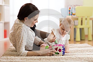 Mother and baby girl playing with developmental toys in nursery room photo