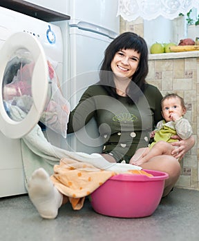 Woman with baby putting clothes in to washing machine
