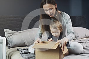 Woman and baby unpacking cardboard box with surprise. International shopping with shipment worldwide