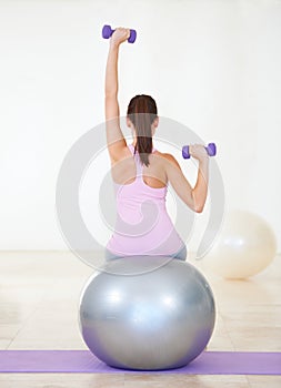 Woman, back and fitness on ball, dumbbells and balance in gym, training and strong muscle in arms. Girl, workout and