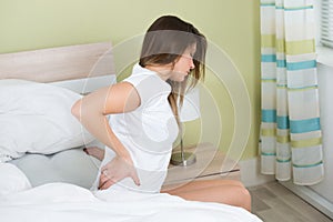 Woman With Back Pain Sitting On Bed