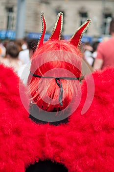 woman on back view wearing with red wings of angel and red hairs walking in the street at the gay pride