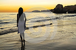 Woman at back with white dress introducing feet in the beach at sunset