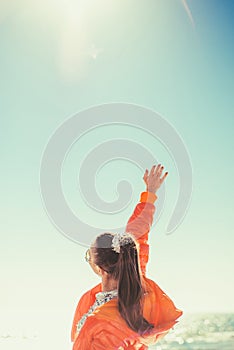 A woman in the background of the sea draws her hand to the sky. Back view