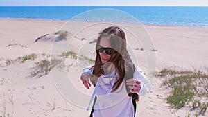 Woman with backpack climbs on sand dune and looks at sea from top on vacation.