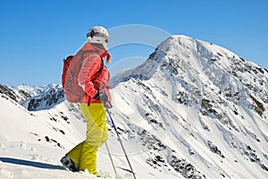 Woman with backpack, helmet, and ski poles looks towards Parpaner Rothorn peak and ridge. Breathtaking views in Swiss Alps