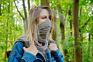 Woman with backpack hide face with a scarf in forest