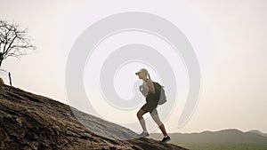 Woman with backpack hikes up mountain at dawn. Silhouette against rising sun, active lifestyle. Female climber conquers