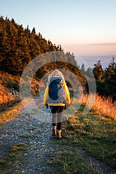 Woman with backpack hiking on mountain trail during sunset at autumn