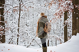 Woman with backpack hiking in snow at winter woodland