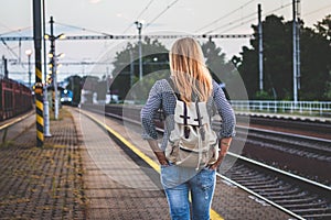 Woman with backpack is looking at arriving train at a railway station