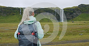 Woman with backpack looking at Seljalandsfoss waterfall Iceland