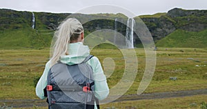 Woman with backpack looking at Seljalandsfoss waterfall Iceland