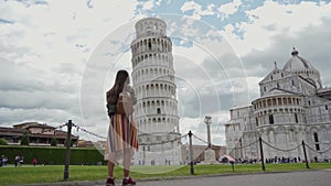 Woman with backpack looks at Leaning Tower, smiles to camera General view. Sunny