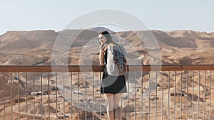 Woman with backpack looks at massive mountain view. Pretty Caucasian girl enjoys incredible desert panorama. Israel 4K.