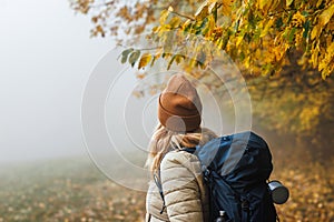 Woman with backpack lost her way in fog during trekking in autumn woodland