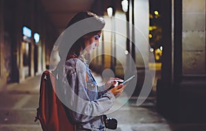 Woman with backpack pointing finger on blank screen smartphone on background bokeh light in night atmospheric city, blogger