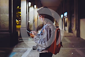 Woman with backpack pointing finger on blank screen smartphone on background bokeh light in night atmospheric city, blogger hipste